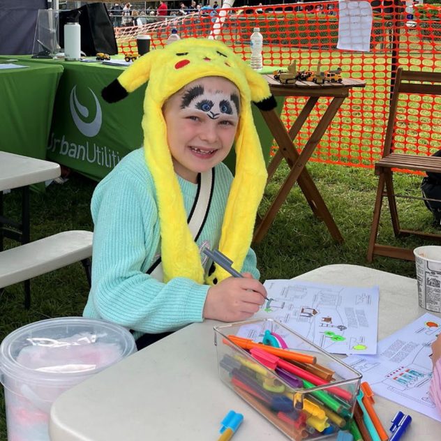 Child with a Pikachu hat coloring happily at the Esk Show.